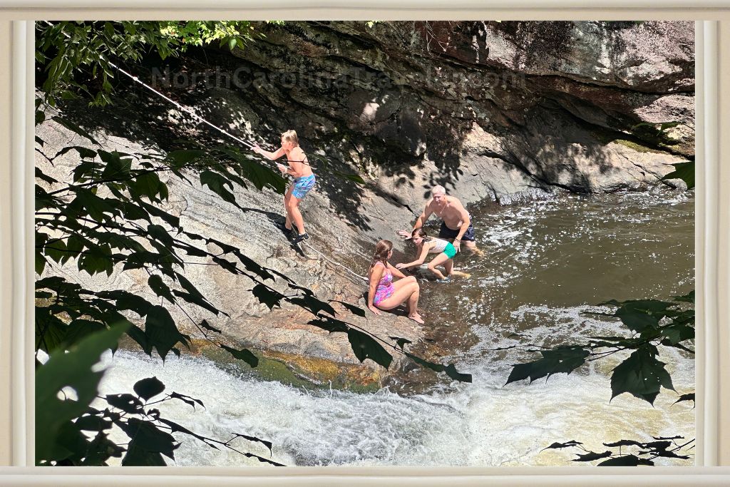 family at bust your butt falls, one kids climbing up the rock with a rope to slide down the waterfall from the top